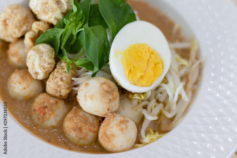 Thai Food. Rice Noodles in Fish Curry With boiled egg, fish balls, pork snack, basil, bean sprouts on top, placed on a wooden table. Thai Food. Rice Noodles in Fish Curry With boiled egg, fish balls, pork snack, basil, bean sprouts on top, placed on a wooden table.