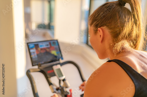 Fitness workout woman training at home on smart stationary bike equipment connected online live streaming class indoors for biking exercise. Indoor cycling. Focus on the sweat on person's back. photo