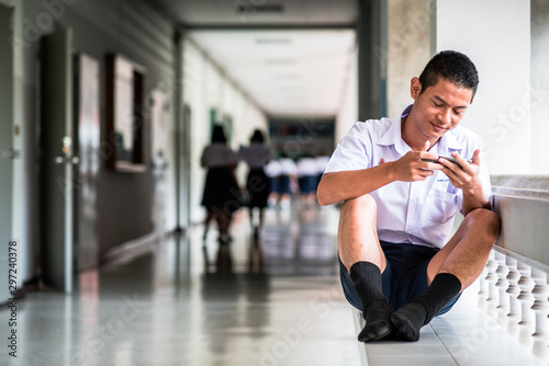 Asian male high school student in a white uniform, who is a lot of addicted to games. He is playing exciting games on their mobile phones and sitting in the school.