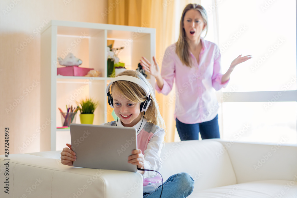 Woman is scolding her teenage daughter, girl is listening to music in headphones and ignoring her mom - obrazy, fototapety, plakaty 