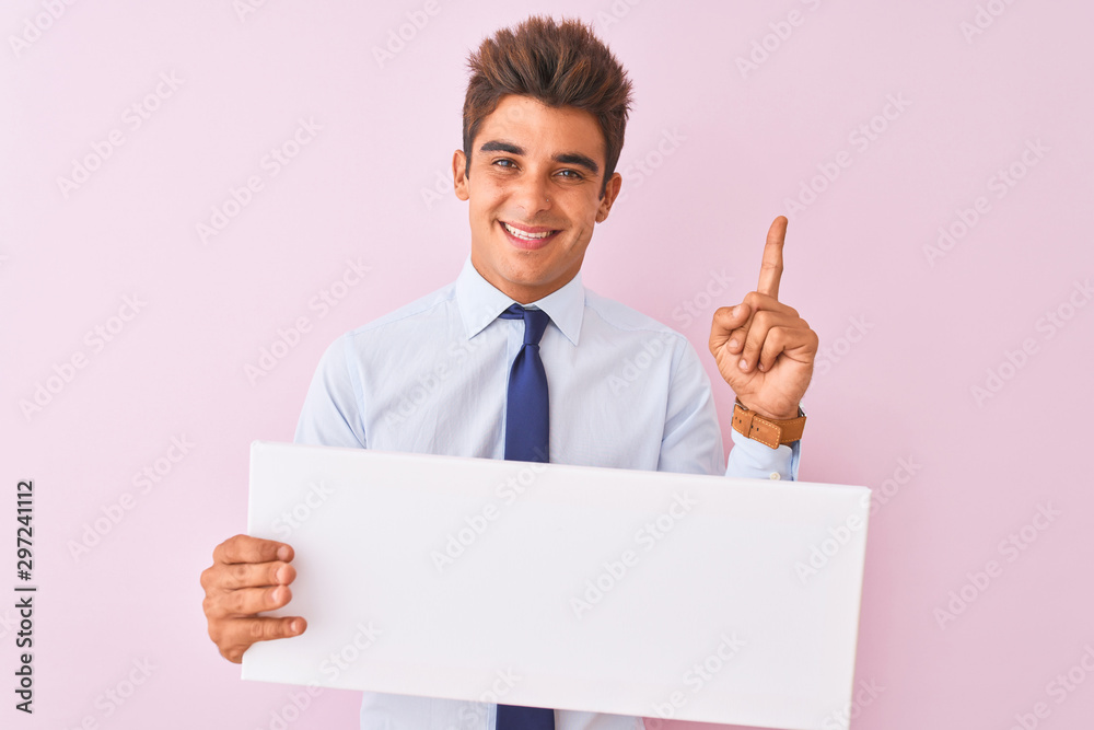 Young handsome businessman holding banner standing over isolated pink background very happy pointing with hand and finger to the side Young handsome businessman holding banner standing over isolated pink background very happy pointing with hand and finger to the side