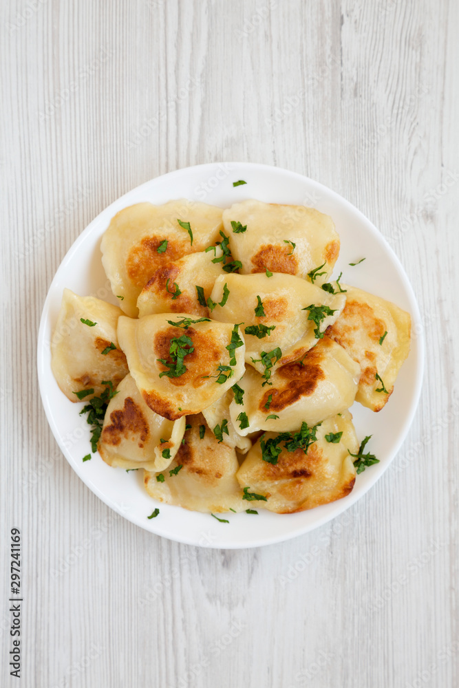 Homemade traditional polish fried potato pierogis on a white plate on a white wooden surface, top view. From above, flat lay, overhead. Homemade traditional polish fried potato pierogis on a white plate on a white wooden surface, top view. From above, flat lay, overhead.