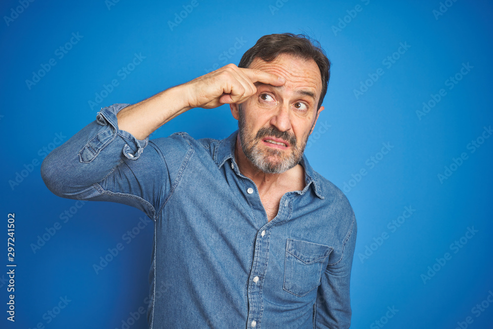 Handsome middle age senior man with grey hair over isolated blue background pointing unhappy to pimple on forehead, ugly infection of blackhead. Acne and skin problem Handsome middle age senior man with grey hair over isolated blue background pointing unhappy to pimple on forehead, ugly infection of blackhead. Acne and skin problem