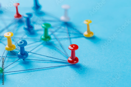Small network of colorful pins and string, An arrangement of colorful pins linked together with string on a blue background suggesting a network of connections.