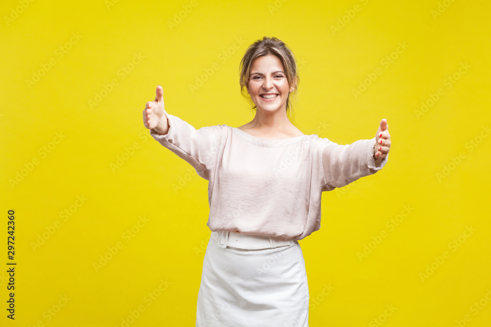 Come into my arms. Portrait of friendly beautiful woman with fair hair in casual beige blouse standing with stretching hands, wants to hug tight. indoor studio shot isolated on yellow background Come into my arms. Portrait of friendly beautiful woman with fair hair in casual beige blouse standing with stretching hands, wants to hug tight. indoor studio shot isolated on yellow background