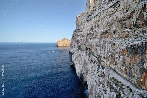panoramic view of the Capo Caccia promontory near the Grotte di Nettuno with the cut on the rock made for the staircase called Escala del Cabirol. The Foradada Island in the background photo