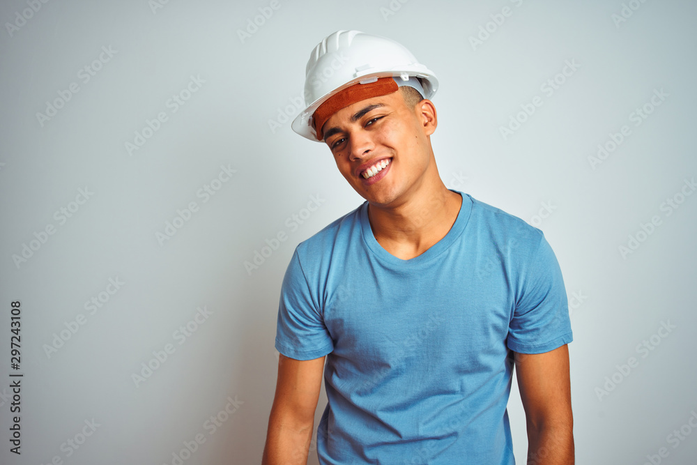 Young brazilian engineer man wearing security helmet standing over isolated white background looking away to side with smile on face, natural expression. Laughing confident.