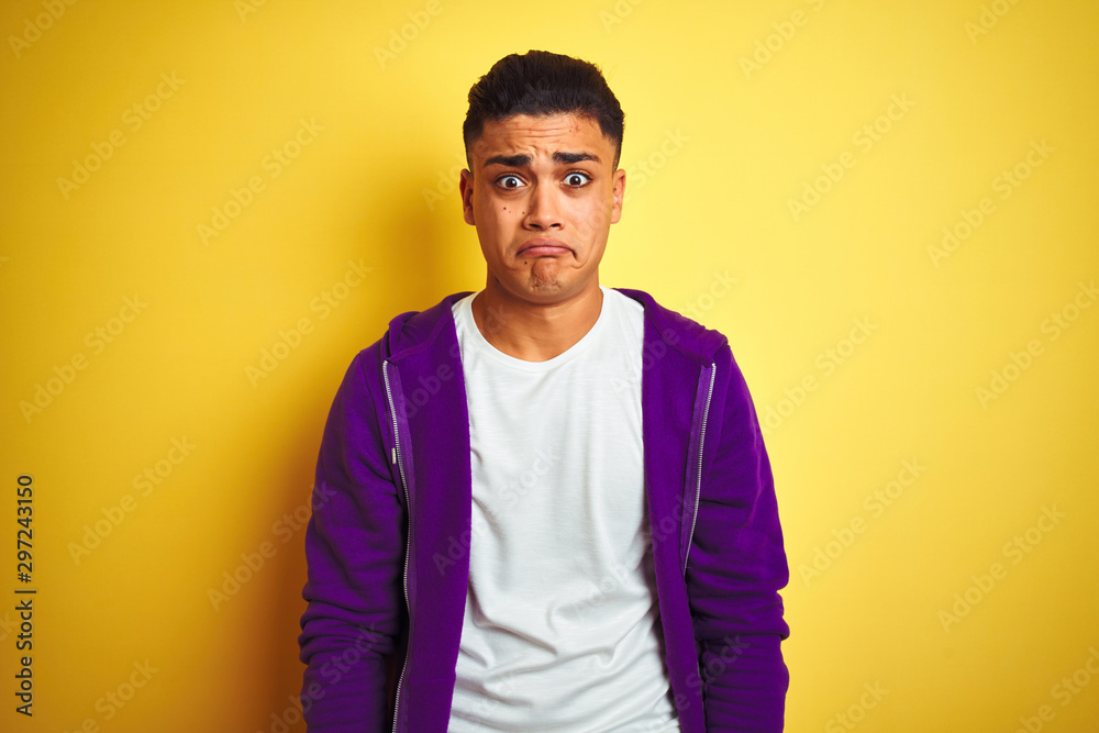 Young brazilian man wearing purple sweatshirt standing over isolated yellow background depressed and worry for distress, crying angry and afraid. Sad expression. - obrazy, fototapety, plakaty 