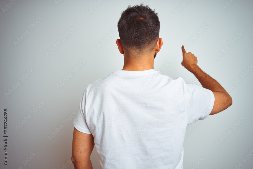 Young indian man wearing t-shirt standing over isolated white background Posing backwards pointing ahead with finger hand Young indian man wearing t-shirt standing over isolated white background Posing backwards pointing ahead with finger hand