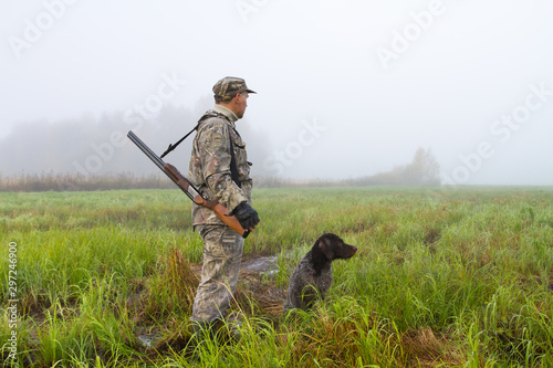 a hunter and his gundog are in a meadow on a foggy morning