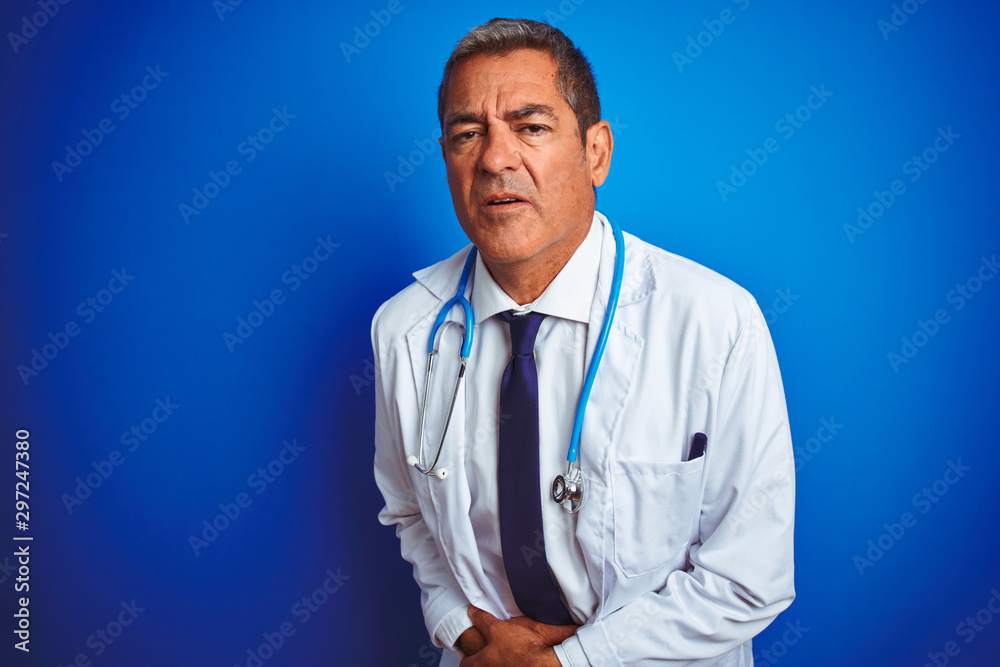 Handsome middle age doctor man wearing stethoscope over isolated blue background with hand on stomach because indigestion, painful illness feeling unwell. Ache concept. Handsome middle age doctor man wearing stethoscope over isolated blue background with hand on stomach because indigestion, painful illness feeling unwell. Ache concept.