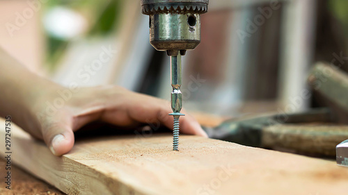 The carpenter uses a drill to tighten the screws to the plank.