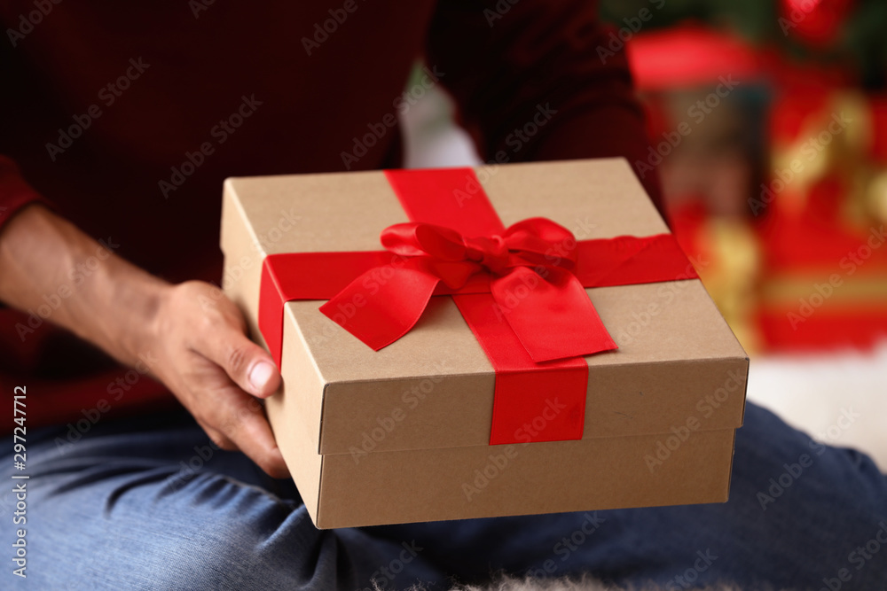 Man in red sweater holding Christmas gift at home, closeup