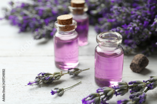 Bottles with essential oil and lavender flowers on white wooden table
