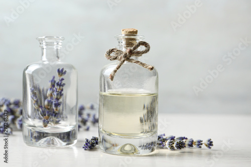 Bottles with natural essential oil and lavender flowers on white wooden table