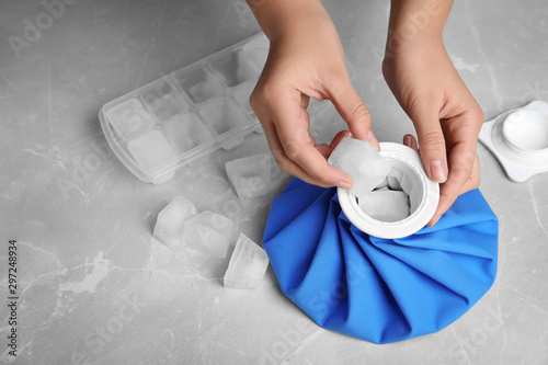 Woman putting ice cubes into pack at marble table, closeup photo