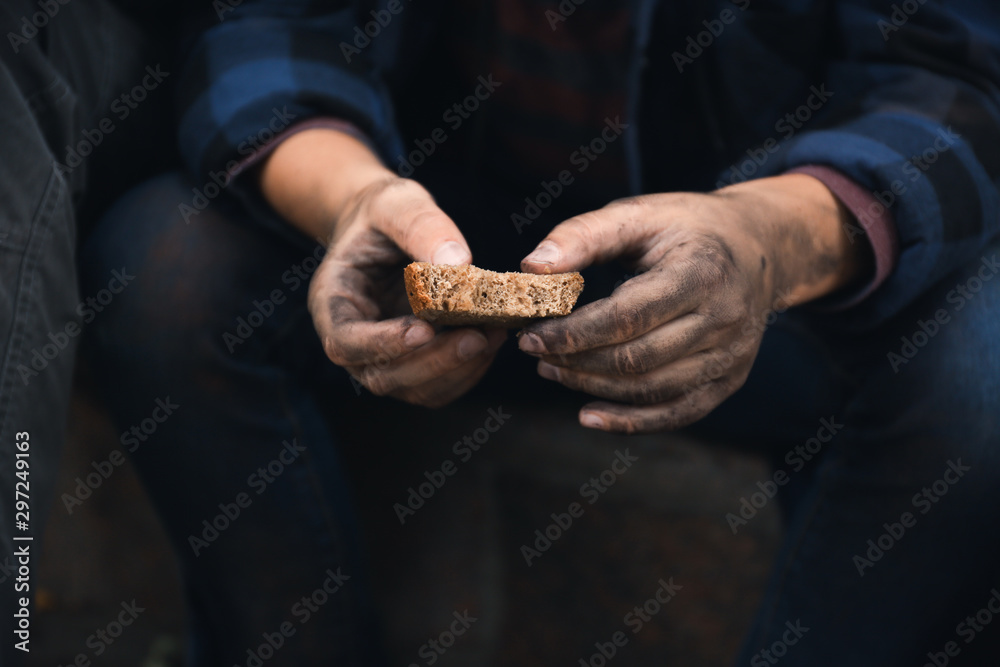 Poor homeless with piece of bread outdoors, closeup
