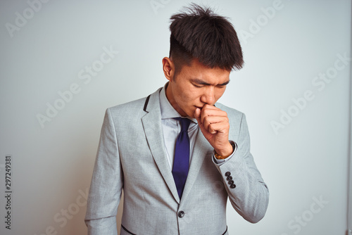 Asian chinese businessman wearing suit and tie standing over isolated yellow background feeling unwell and coughing as symptom for cold or bronchitis. Healthcare concept.