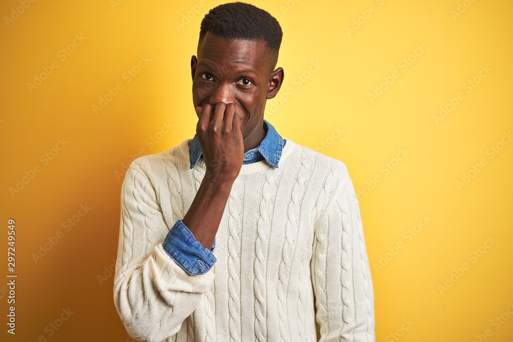 African american man wearing denim shirt and white sweater over isolated yellow background looking stressed and nervous with hands on mouth biting nails. Anxiety problem.
