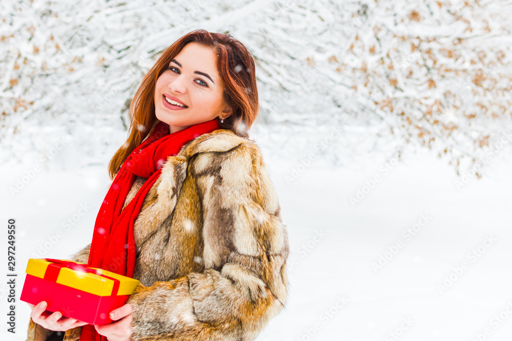 beautiful smiling woman holding a gift box on a snowy forest background beautiful smiling woman holding a gift box on a snowy forest background