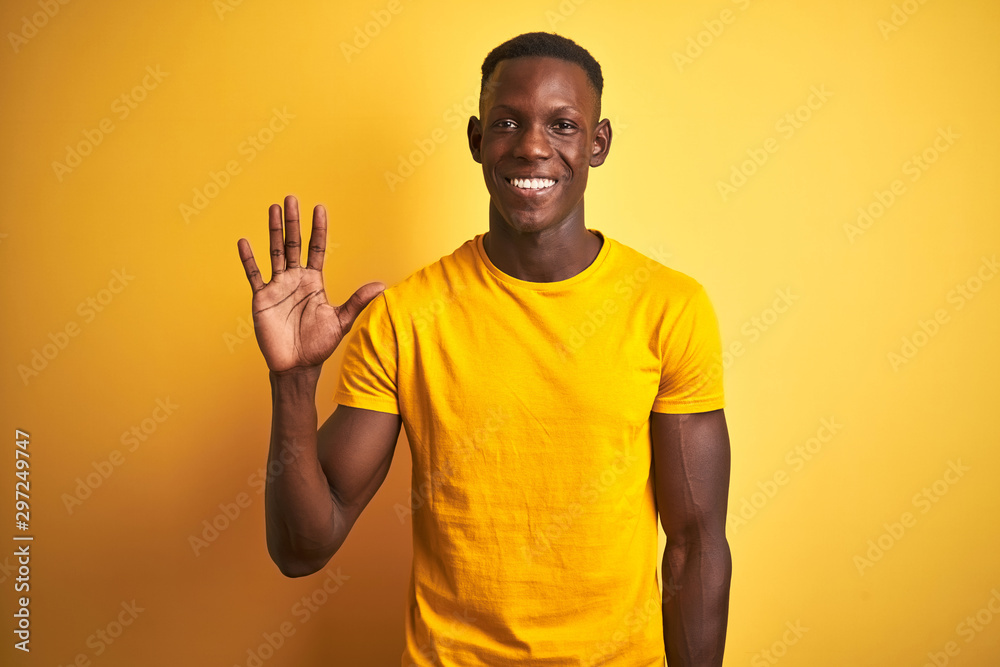Young african american man wearing casual t-shirt standing over isolated yellow background showing and pointing up with fingers number five while smiling confident and happy. Young african american man wearing casual t-shirt standing over isolated yellow background showing and pointing up with fingers number five while smiling confident and happy.