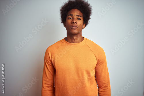 Young american man with afro hair wearing orange sweater over isolated white background with serious expression on face. Simple and natural looking at the camera.