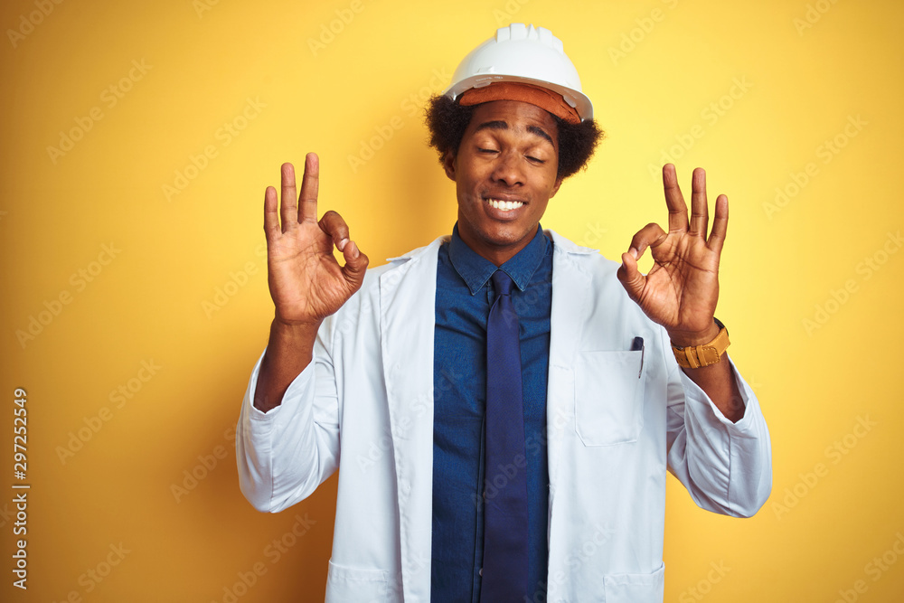 Afro american engineer man wearing white coat and helmet over isolated yellow background relax and smiling with eyes closed doing meditation gesture with fingers. Yoga concept.