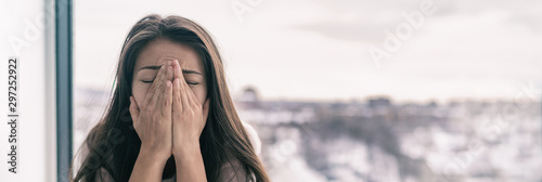 Sad upset young woman crying with mental health seasonal affective disorder at home breathing in hands panoramic background banner. Winter blues. photo