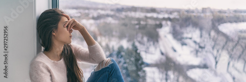 Winter depression sad woman with Seasonal affective disorder girl grief stricken alone at home window thinking negative thoughts. Mental health banner panorama background.