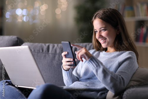 Happy woman using laptop checks smart phone