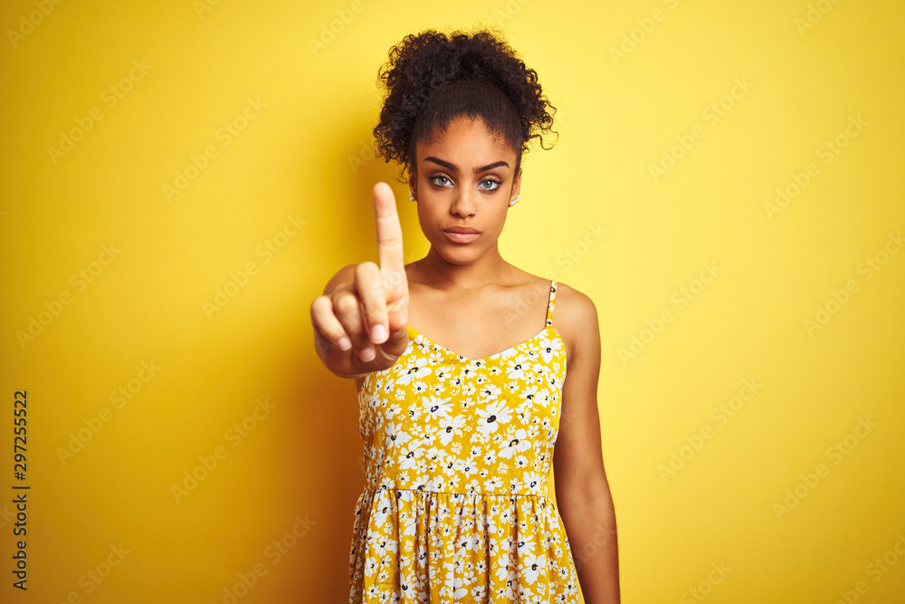 African american woman wearing casual floral dress standing over isolated yellow background Pointing with finger up and angry expression, showing no gesture African american woman wearing casual floral dress standing over isolated yellow background Pointing with finger up and angry expression, showing no gesture