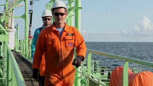 tanker ship workers wearing bright protective jumpsuits walk along ship deck between green constructions close view
