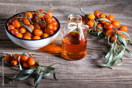 Sea buckthorn berries on a branch, in a white Cup and a bottle of sea buckthorn oil on a wooden table.