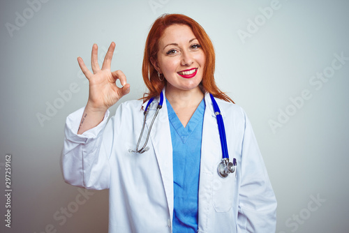 Young redhead doctor woman using stethoscope over white isolated background smiling positive doing ok sign with hand and fingers. Successful expression.