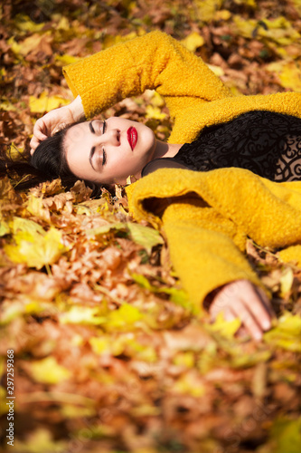 Beautiful woman lying on yellow leaves in park. Leisure time on warm autumn day.