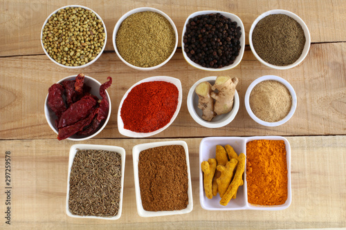 Indian Spices, like coriander, pepper, red chili, ginger, turmeric, and cumin, and their freshly ground powders, arranged as pairs in bowls, on a wooden background.