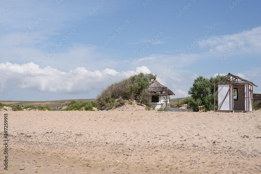 Sandy seashore, blue sky with clouds and abandoned bungalow Sandy seashore, blue sky with clouds and abandoned bungalow