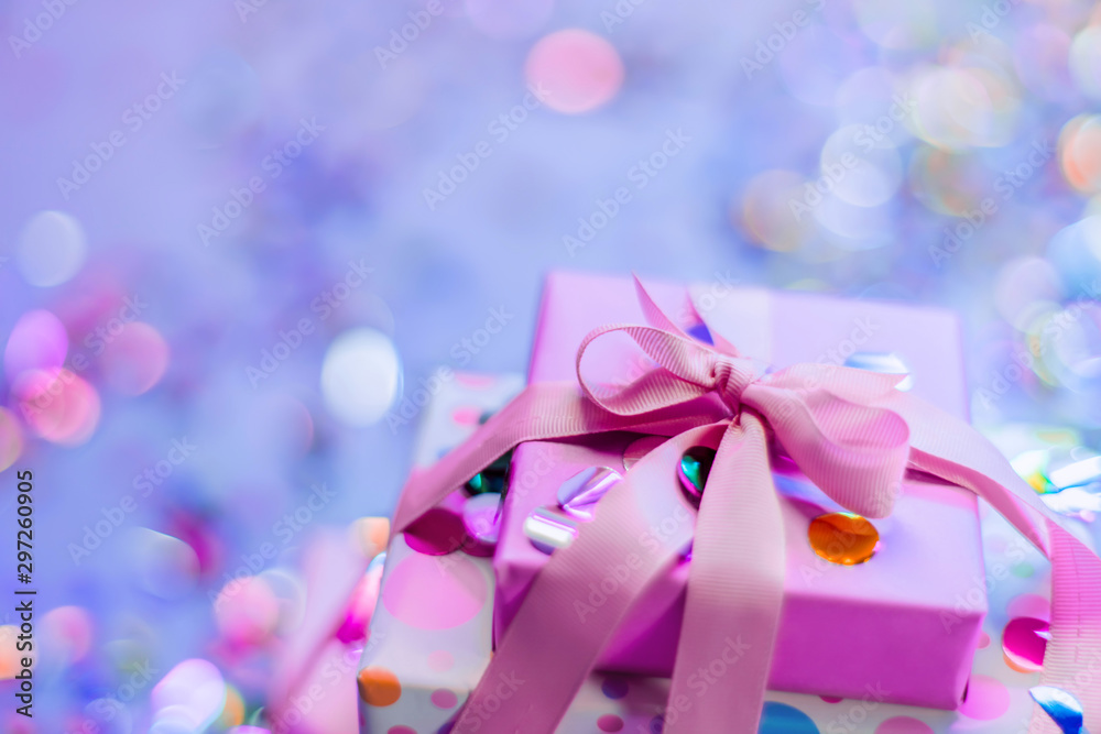 Beautifully packaged gifts on a background of shiny confetti. Neon party light. Pink ribbon. Gifts for Christmas, new year, birthday. Fun party. Photographed close-up Beautifully packaged gifts on a background of shiny confetti. Neon party light. Pink ribbon. Gifts for Christmas, new year, birthday. Fun party. Photographed close-up