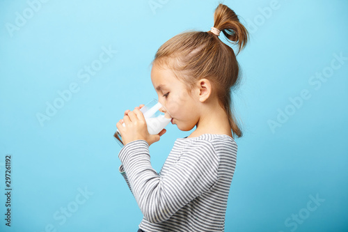 фотографія Child girl drinks milk without lactose, sideways portrait against blue isolated