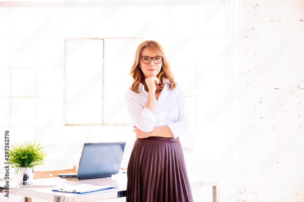 Confident middle aged businesswoman portrait while standing at office desk Confident middle aged businesswoman portrait while standing at office desk