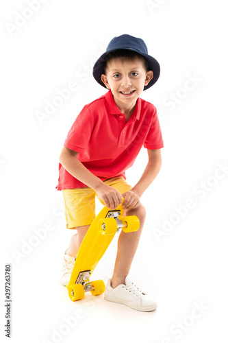 A little boy in panama, yellow jersey, red shorts and white sneakers stands and holds a yellow penny