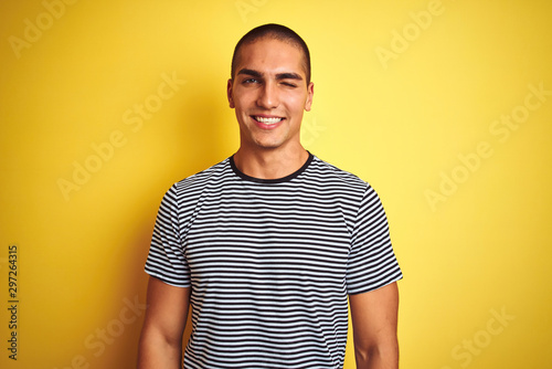 Young handsome man wearing striped t-shirt over yellow isolated background winking looking at the camera with sexy expression, cheerful and happy face.