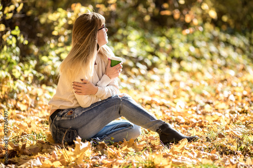 girl sits and relax on the ground in the autumn forest with coffee