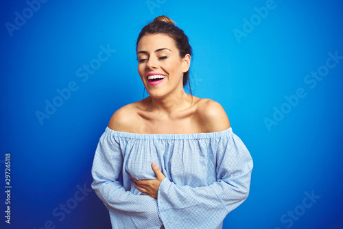 Young beautiful woman wearing bun hairstyle over blue isolated background smiling and laughing hard out loud because funny crazy joke with hands on body.