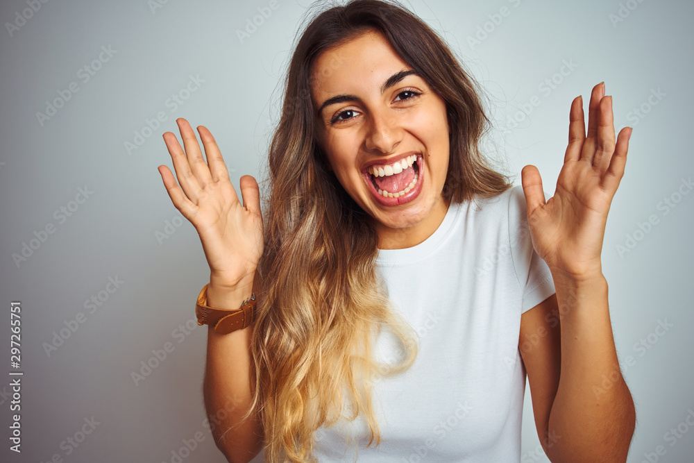 Young beautiful woman wearing t-shirt over white isolated background very happy and excited, winner expression celebrating victory screaming with big smile and raised hands Young beautiful woman wearing t-shirt over white isolated background very happy and excited, winner expression celebrating victory screaming with big smile and raised hands