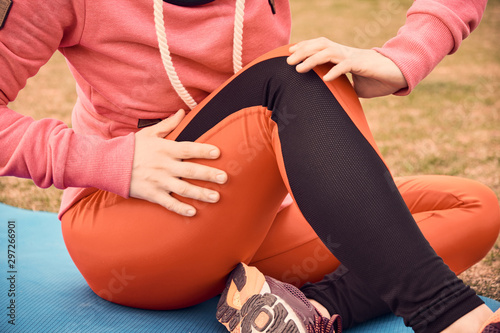 Female athlete suffering form running knee or kneecap injury during outdoor workout on dirt road.