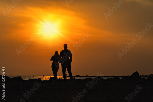 silhouettes of man and woman on a dais stand with their backs and look at sea sunset