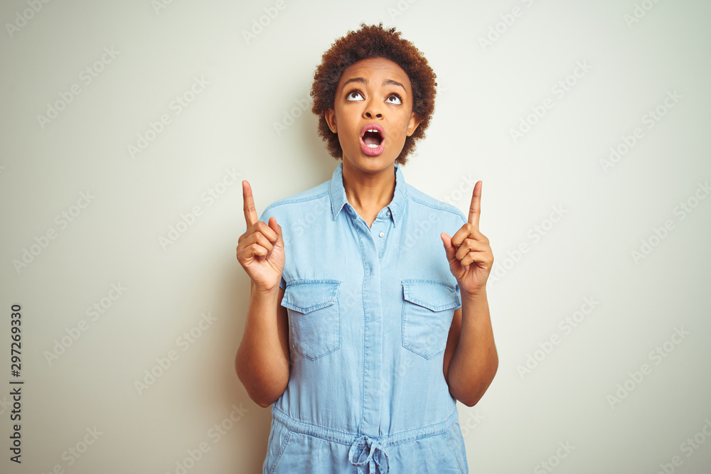 Young beautiful african american woman with afro hair over isolated background amazed and surprised looking up and pointing with fingers and raised arms.