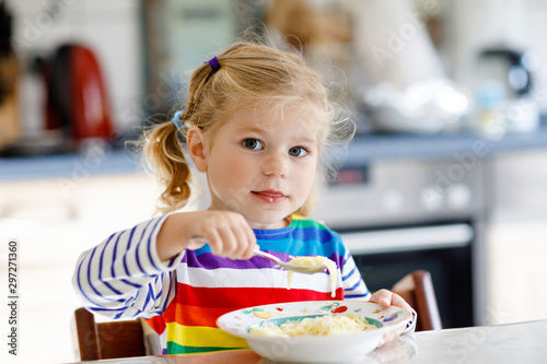 Adorable toddler girl eating healthy chicken noodle soup for lunch. Cute happy baby child taking food at home or nursery daycare or kindergarten and learning using spoon.
