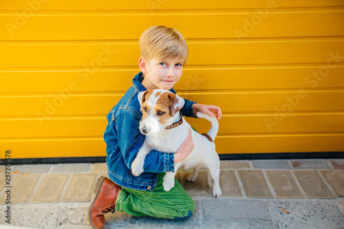 Preteen boy playing and talking with hid dog Jack Russell Terrier on yeloow background outdoor. Friendship relationship feeling concept. Dog protect owner. photo